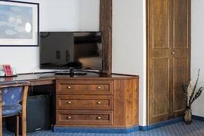 A hotel room with a wooden desk, a television, a chair, a wardrobe, and a framed picture on the wall. - Hotel Goldener Hirsch (Kaufbeuren)