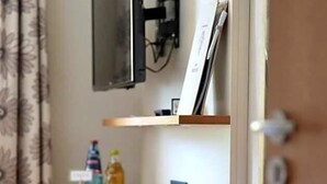 Ein Zimmer mit einem Holztisch, einem roten Kissen, einem an der Wand montierten Fernseher und einem Regal mit Flaschen.
