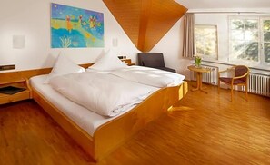 A hotel room with a wooden bed, a small table with a chair, a painting on the wall, and a window with curtains. - Gasthof Schweizerhof (Villingen-Schwenningen)
