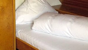 Ein Einzelbett mit weißer Bettwäsche in einem Raum mit Holzwänden und einer schrägen Decke.
