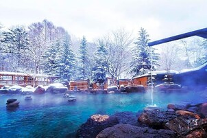 A hot spring area with wooden structures, trees, and a clear blue pool.