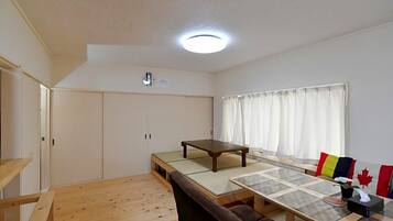 A room with a tatami mat table, a sofa, a window with curtains, and a ceiling light.