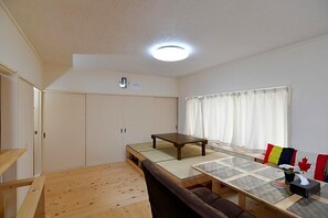 A room with a tatami mat table, a sofa, a window with curtains, and a ceiling light. - Stay In Otaki (Date)