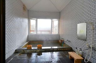 A small, tiled room with a window, a bench, and a shower area.
