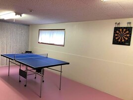 Una habitación con mesa de ping pong, dardos y una ventana con cortinas.