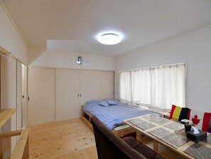 A compact room with a bed, a small table, and a window with curtains. - Stay In Otaki (Date)