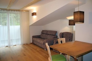 A room with a wooden floor, a sofa, a dining table, and a window with sheer curtains. - Gasthof Majestic (Bressanone)