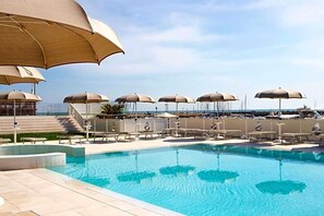 Zona de piscina con sombrillas, sillas de descanso y vista al mar.