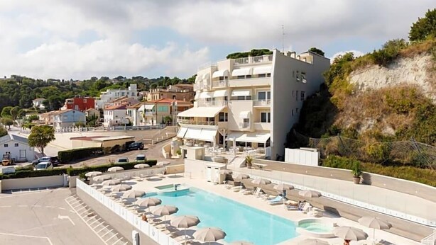 A hotel with a swimming pool, outdoor seating, and a view of the surrounding area. - Hotel Scogliera (Numana)