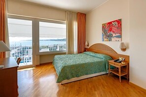Habitación de hotel con cama, escritorio, silla, mesita de noche, lámpara y un cuadro.