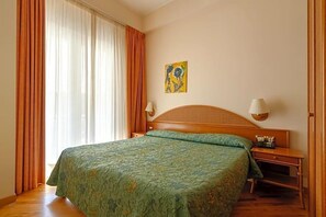 A hotel room with a bed, a nightstand, a lamp, and a painting on the wall. - Hotel Scogliera (Numana)