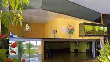 Un hall d’hôtel moderne avec un comptoir d’accueil, un grand aquarium et des plantes d’intérieur.