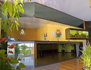 Een moderne hotellobby met een receptiebalie, een groot aquarium en kamerplanten.