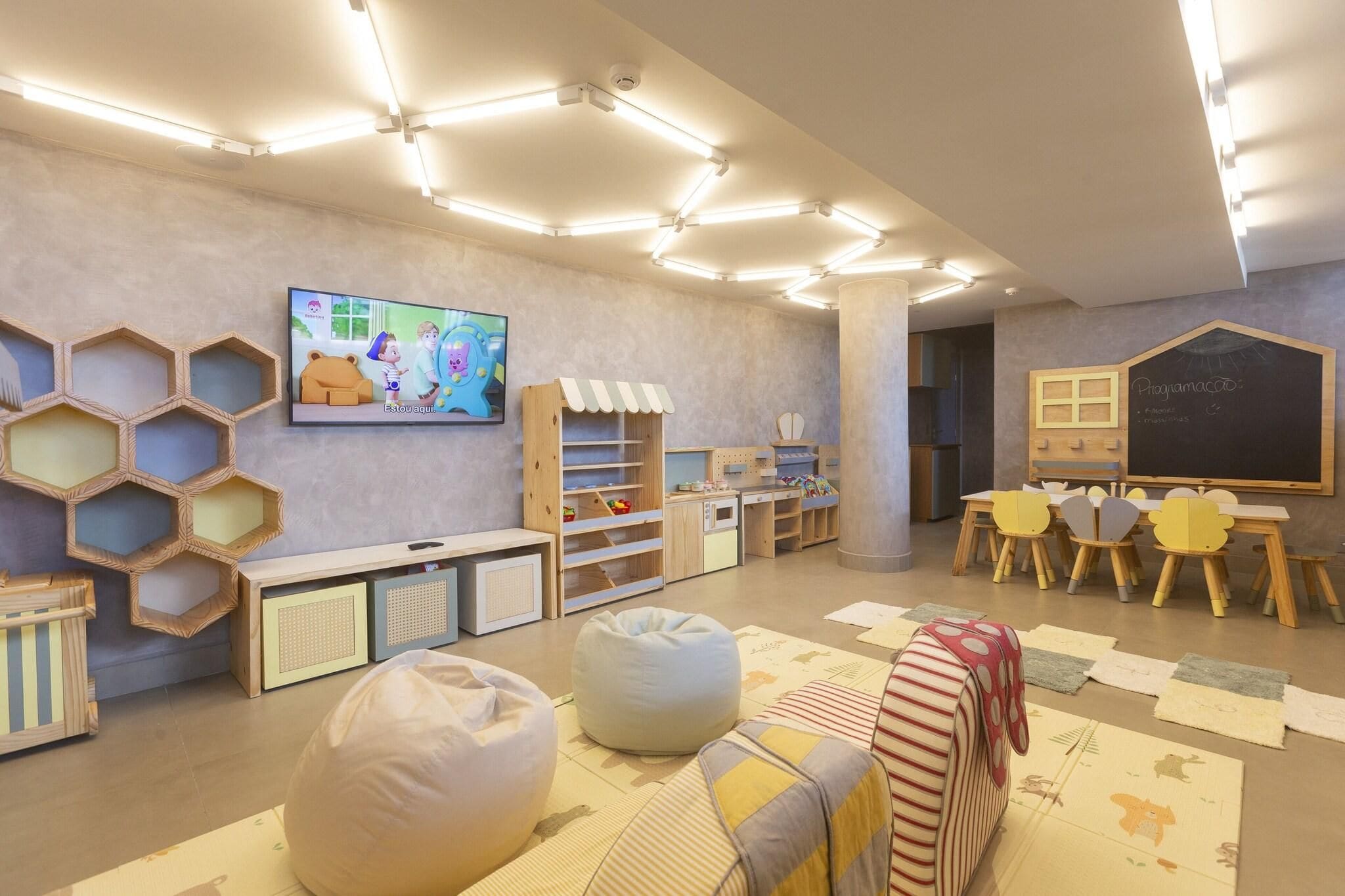 Zona de juegos infantiles con unidades de almacenamiento hexagonales, pufs y una televisión mostrando un programa animado.