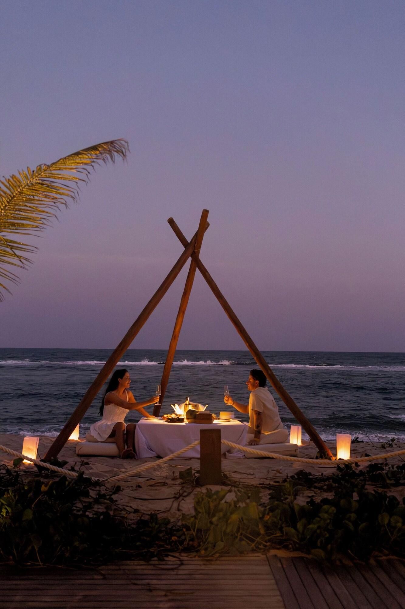 A beachside dining setup with a table and candles, overlooking the ocean.