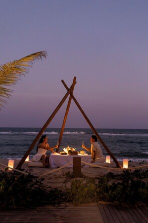 A beachside dining setup with a table and candles, overlooking the ocean. - Ritz Barra De São Miguel (Maceió)