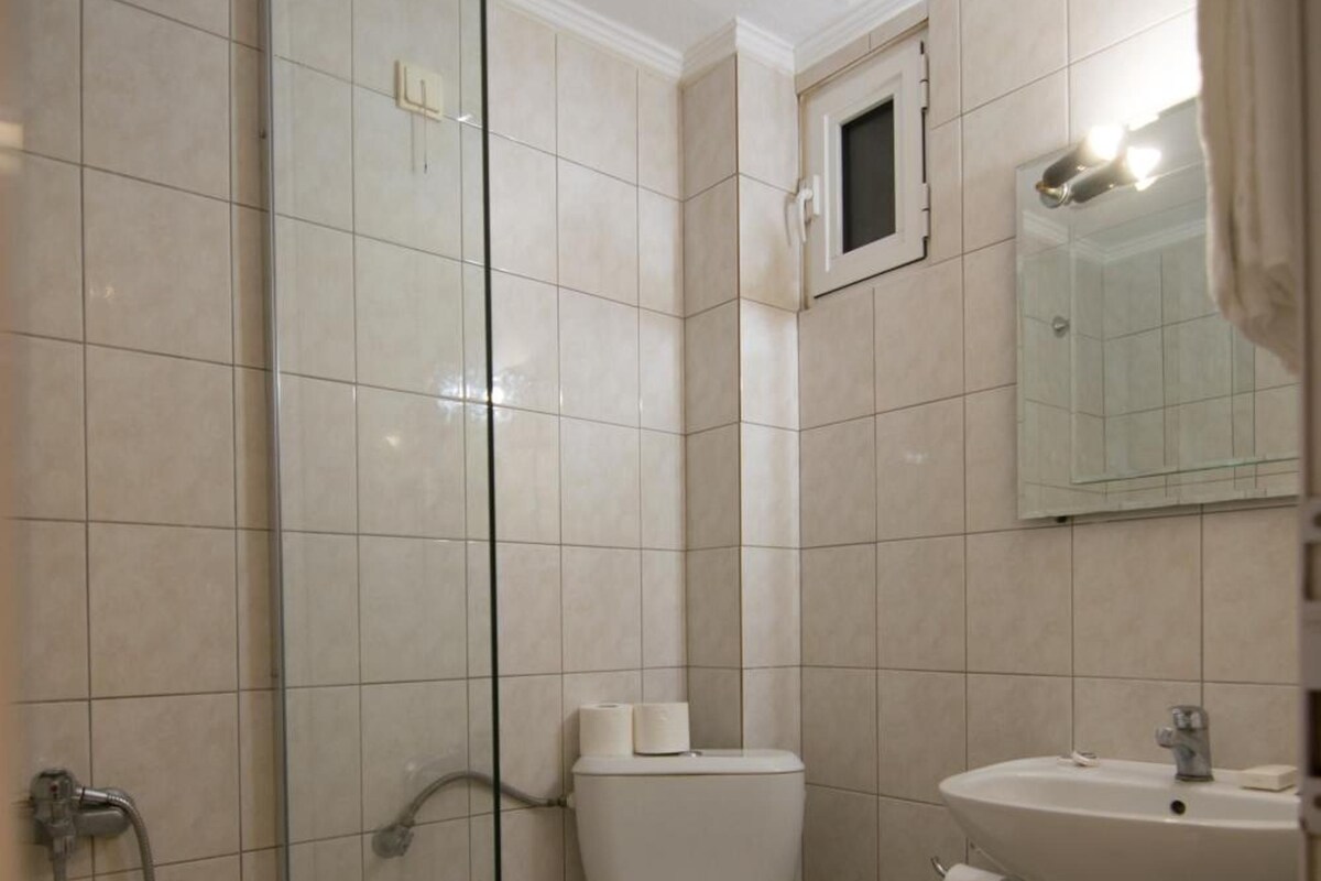 A bathroom with a glass shower enclosure, a toilet, a sink, and a small trash bin.