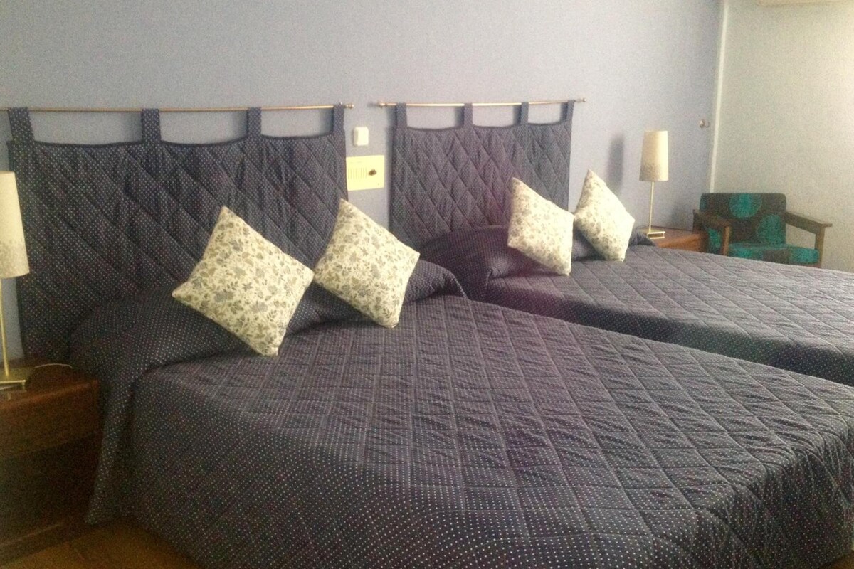 A hotel room with two beds, each with a quilted headboard and matching pillows.