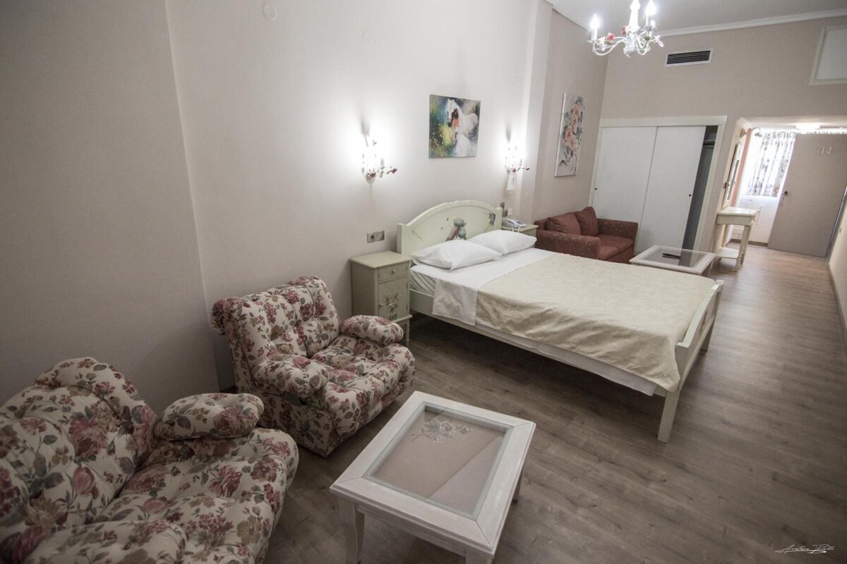 A bedroom with a bed, two chairs, a bedside table, a dresser, and a mirror.