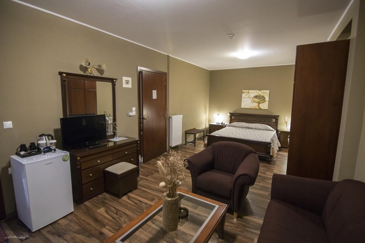 Habitación de hotel con cama, televisor, escritorio con computadora, silla y refrigerador pequeño.