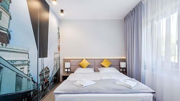 A hotel room with a bed, two pillows, a nightstand, and a wall mural. - Meet Pozna N Hotel (Poznań)