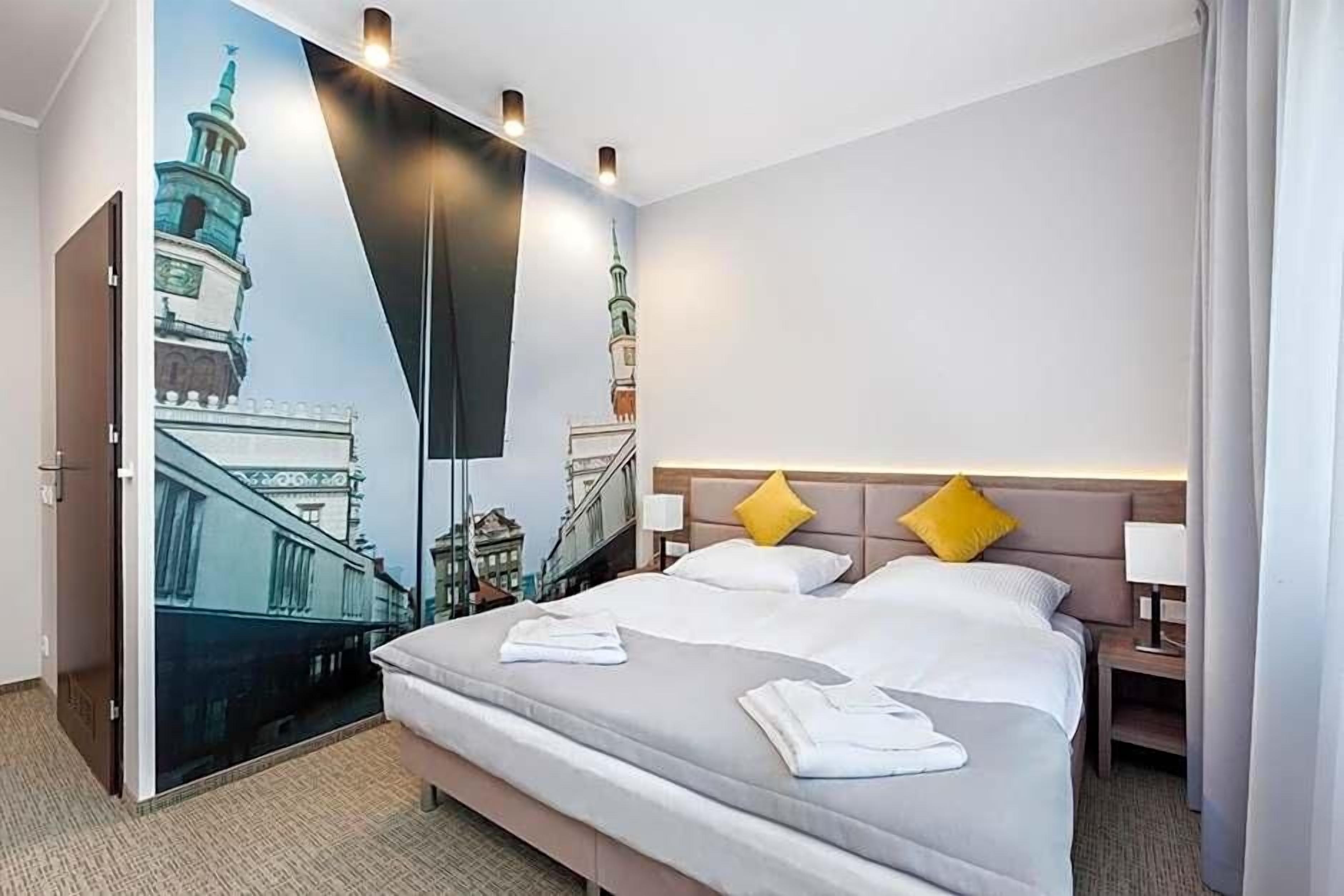 A hotel room with a large bed, two pillows, a nightstand, and a wall mural of a building.