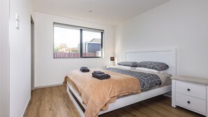A bedroom with a bed, bedside table, and a window. - Spacious Hornby Stay | 3BR | Sleeps 8 | Garage (Christchurch)