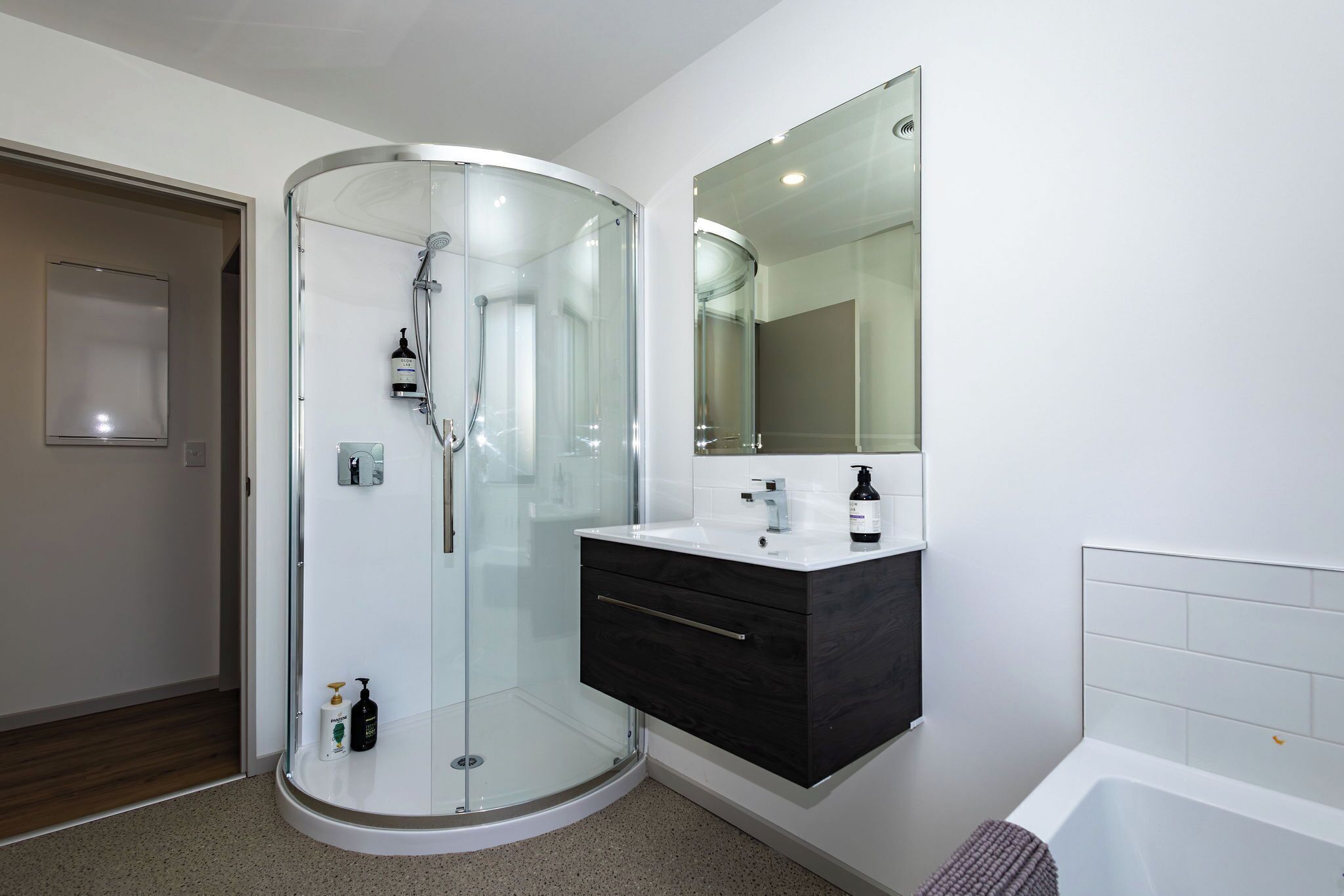 A modern bathroom with a glass-enclosed shower, a white sink with a black cabinet, and a large mirror above the sink.