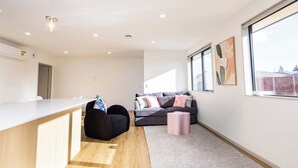 A modern living space with a kitchen area, a sofa set, and large windows. - Spacious Hornby Stay | 3BR | Sleeps 8 | Garage (Christchurch)