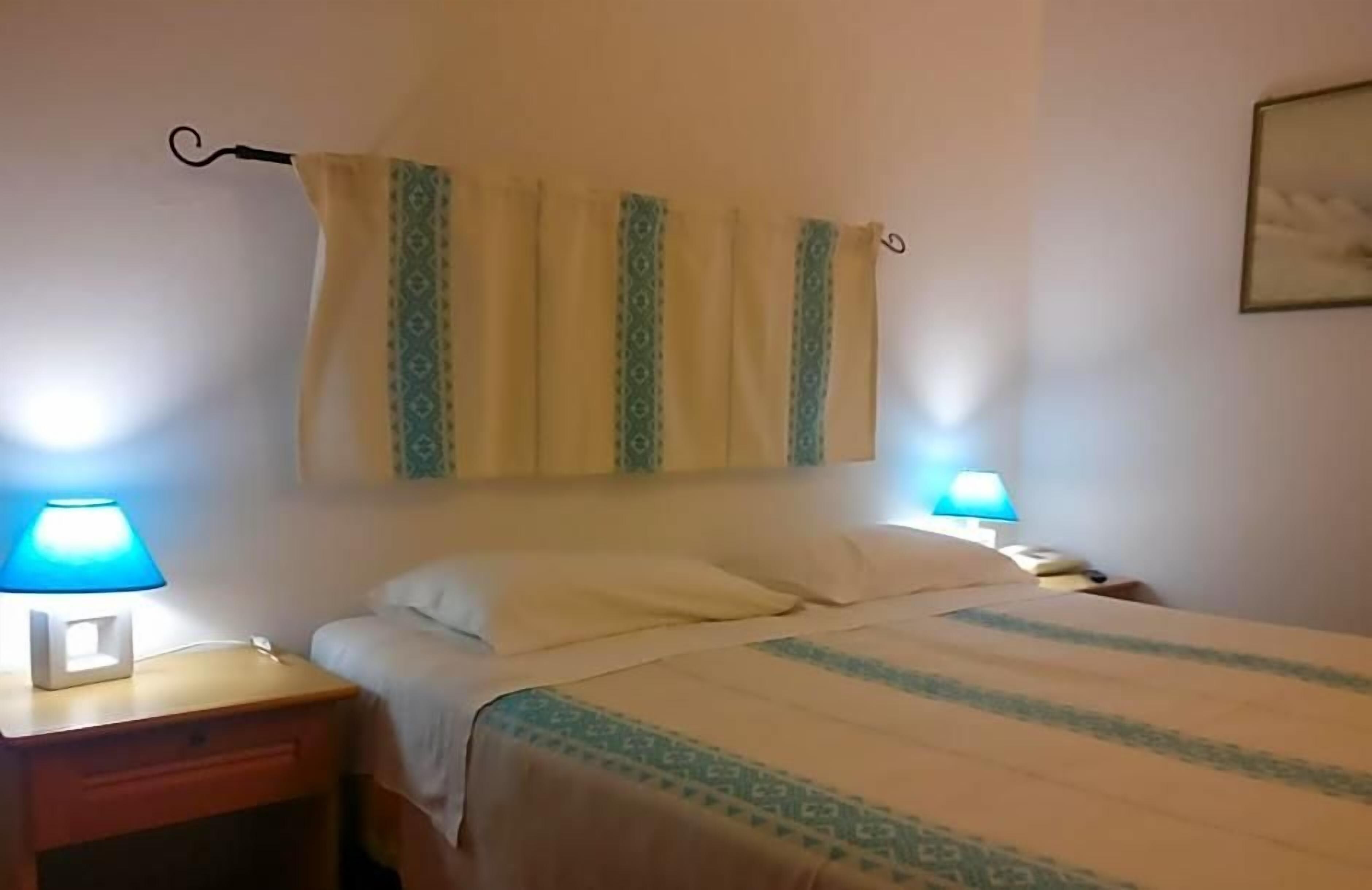 A hotel room with a bed, two bedside lamps, a nightstand, and a curtain.