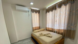 A single bed with a wooden frame, a wall-mounted air conditioner, and a window with patterned curtains.