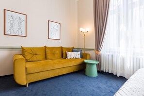 Quarto com sofá, uma mesinha redonda e duas obras de arte penduradas na parede.