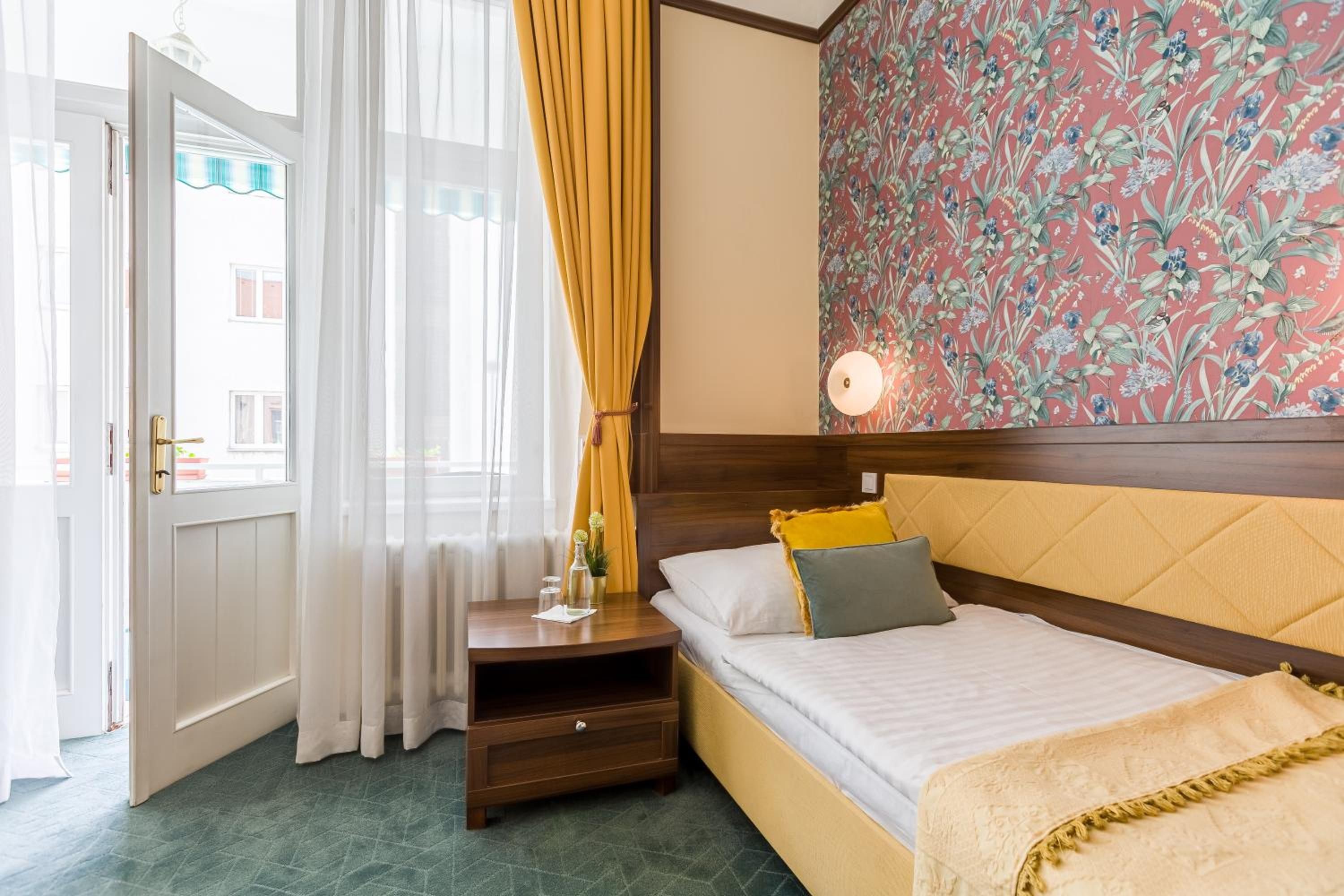 Ein Hotelzimmer mit einem Bett, einem Nachttisch, einer Lampe und einem Fenster mit Vorhängen.