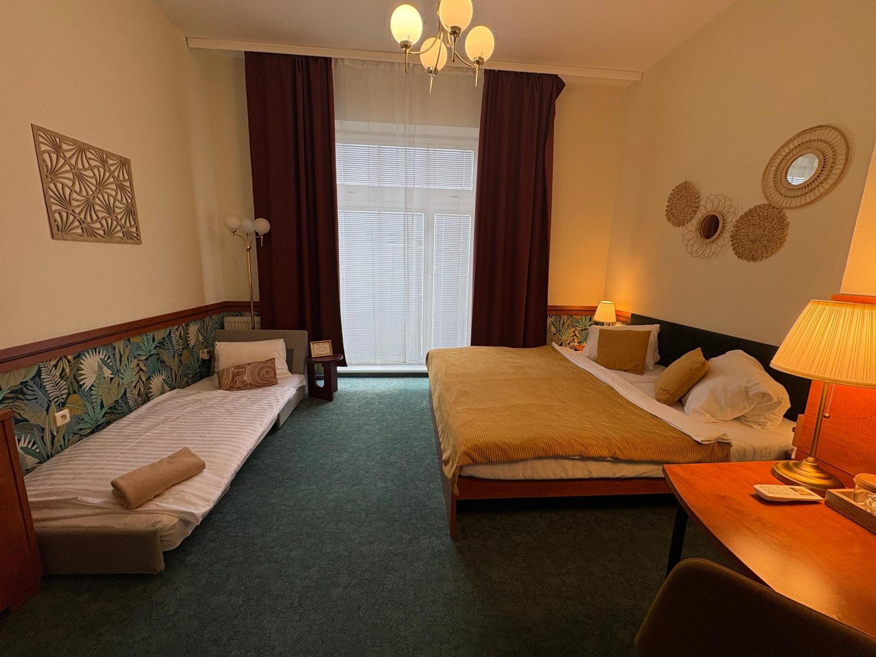 Habitación de hotel con dos camas individuales, un escritorio con silla, una ventana con cortinas y decoración en la pared.