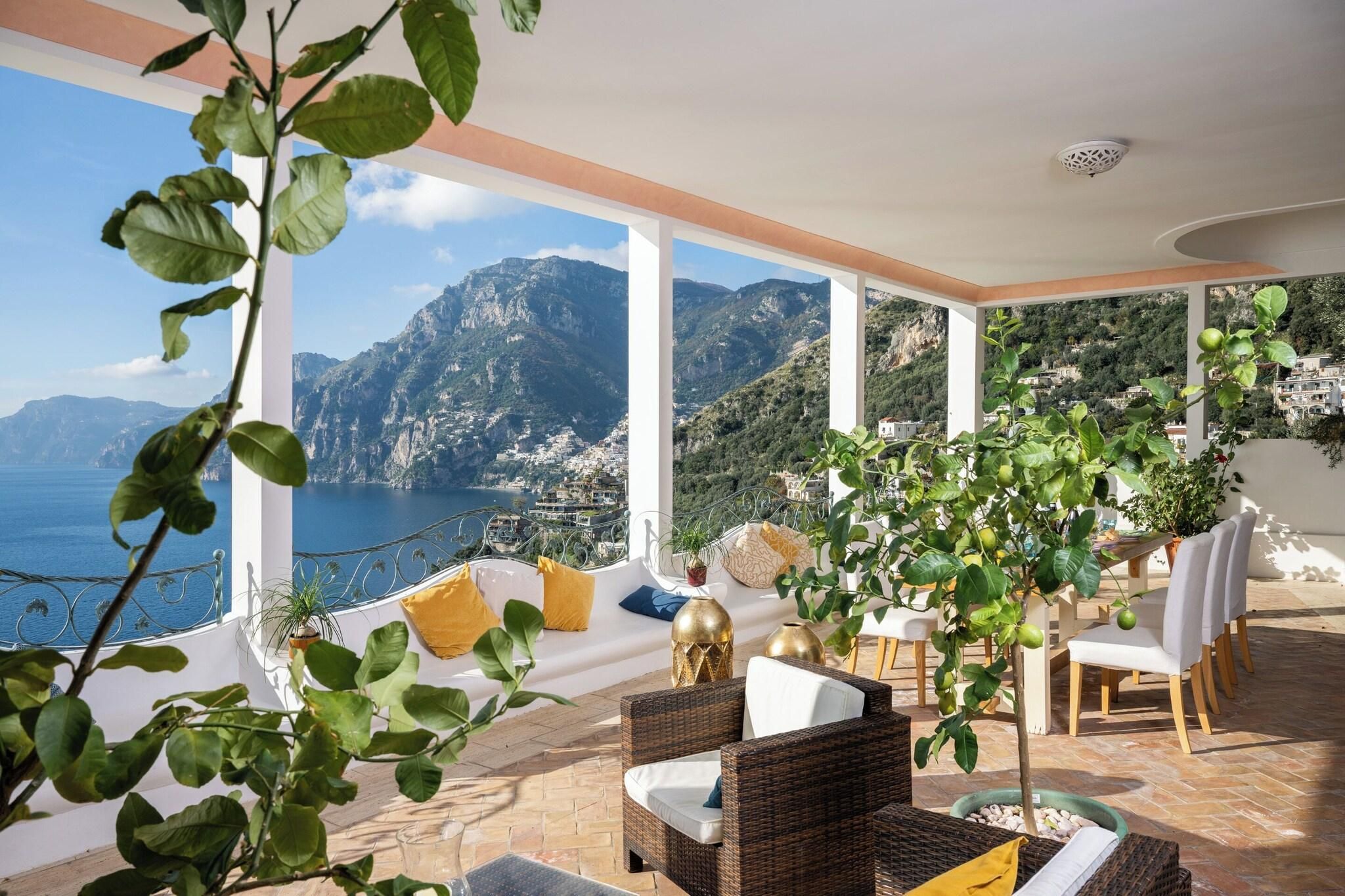 Ein Balkon mit Korbmöbeln, Blick auf das Meer und die Berge sowie Kübelpflanzen.