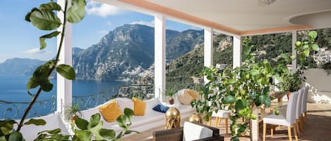 Un balcón con mobiliario de mimbre, vistas al mar y a las montañas, y plantas en macetas.