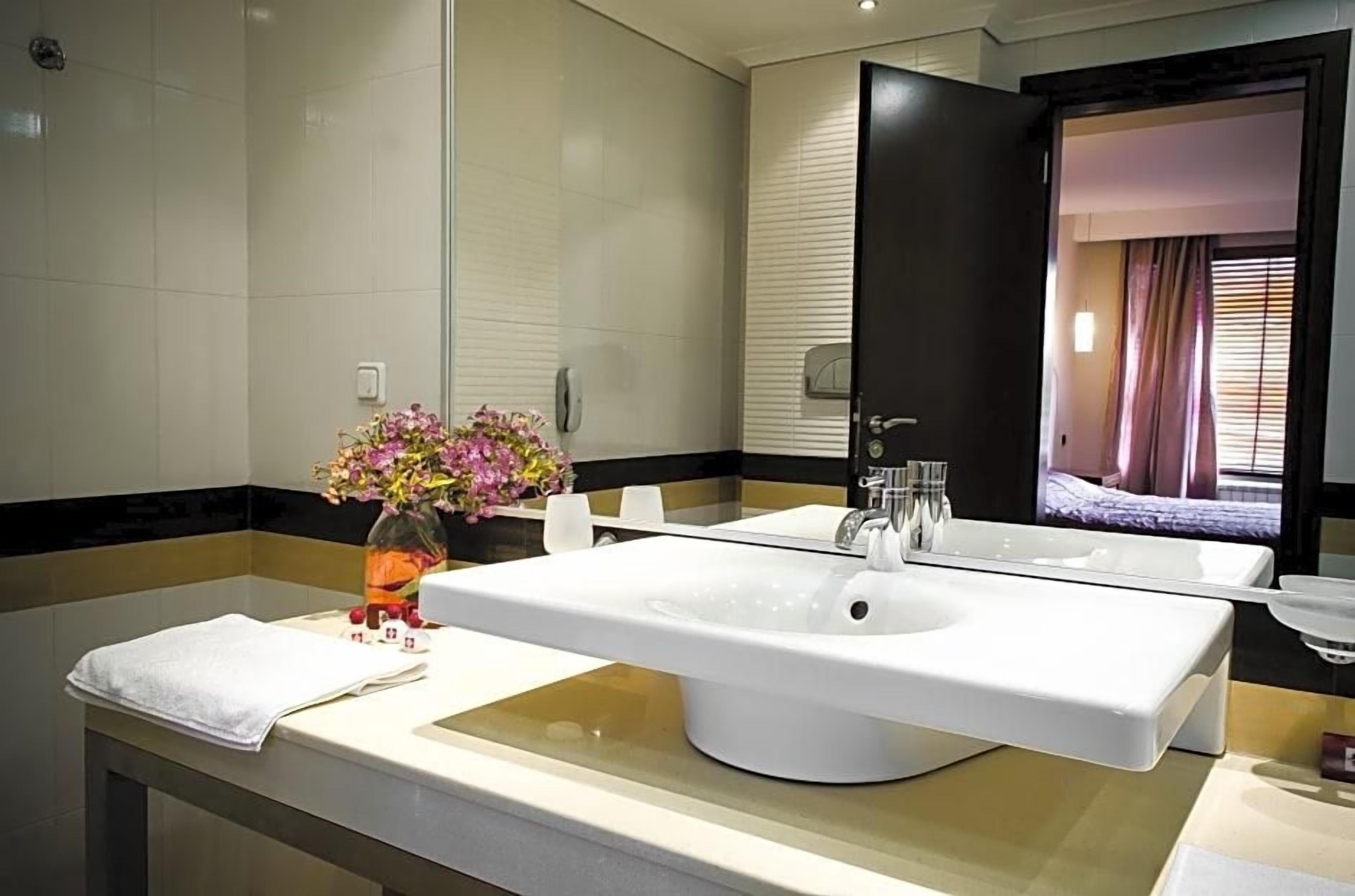 Un baño moderno con un lavabo blanco grande, un espejo y un florero con flores.