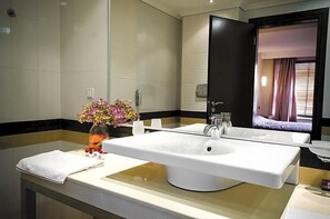 A modern bathroom with a large white sink, a mirror, and a vase of flowers.