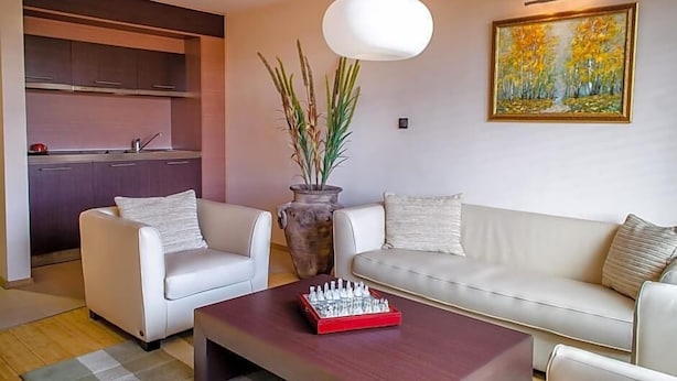 Una sala de estar moderna con un sofá, dos sillones, una mesa de centro, un juego de ajedrez, un jarrón con plantas y un cuadro en la pared.