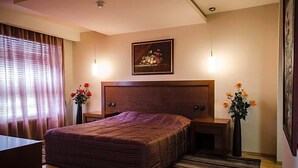 Un dormitorio con una cama grande, mesitas de noche, una obra de arte enmarcada sobre la cama y una ventana con cortinas.