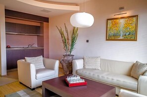 A modern living room with a sofa, two armchairs, a coffee table, a chess set, a vase with plants, and a painting on the wall.