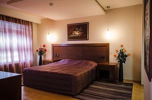 A bedroom with a large bed, bedside tables, a framed artwork above the bed, and a window with curtains.
