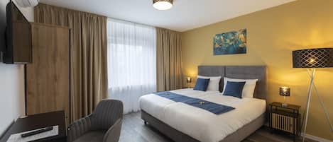 Une chambre d’hôtel avec un lit, un bureau, une chaise, une télévision, une lampe et un tableau au mur.