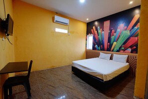 Habitació d'hotel amb un llit, un escriptori, aire condicionat i un mural abstracte i colorit a la paret.