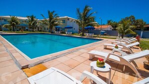 Una piscina con sillas de descanso y sombrillas, rodeada de palmeras y edificios.