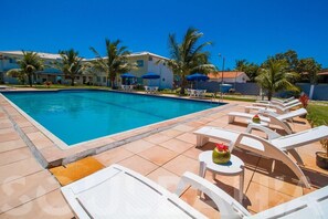 A swimming pool with lounge chairs and umbrellas, surrounded by palm trees and buildings. - Porto Luar Apart Hotel (Porto Seguro)