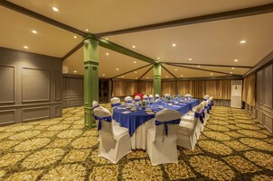 Un salón de conferencias con una larga mesa, sillas blancas adornadas con cintas azules y una alfombra estampada.
