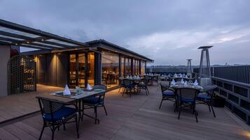 An outdoor dining area with tables and chairs, a covered section with glass walls, and a view of the city skyline.