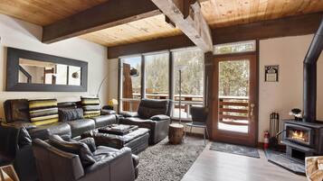 A cozy cabin interior with a fireplace, leather furniture, large windows, and a wooden ceiling.