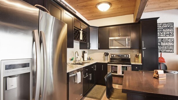 A modern kitchen with stainless steel appliances, dark cabinetry, and a wooden ceiling. - Alpine Manor Retreat (Olympic Valley)